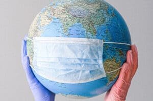 A pair of hands in gloves holding a globe wearing a surgical mask