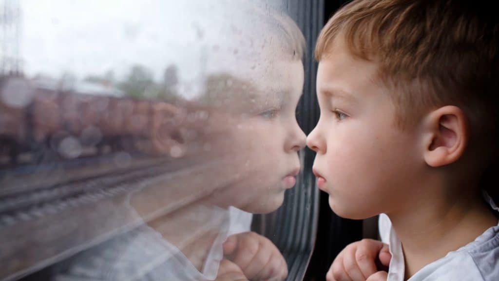 A young boy gazes out of a train window, his reflection mingling with the blurred tracks of the UK countryside in the background, capturing the essence of transport and adventure.