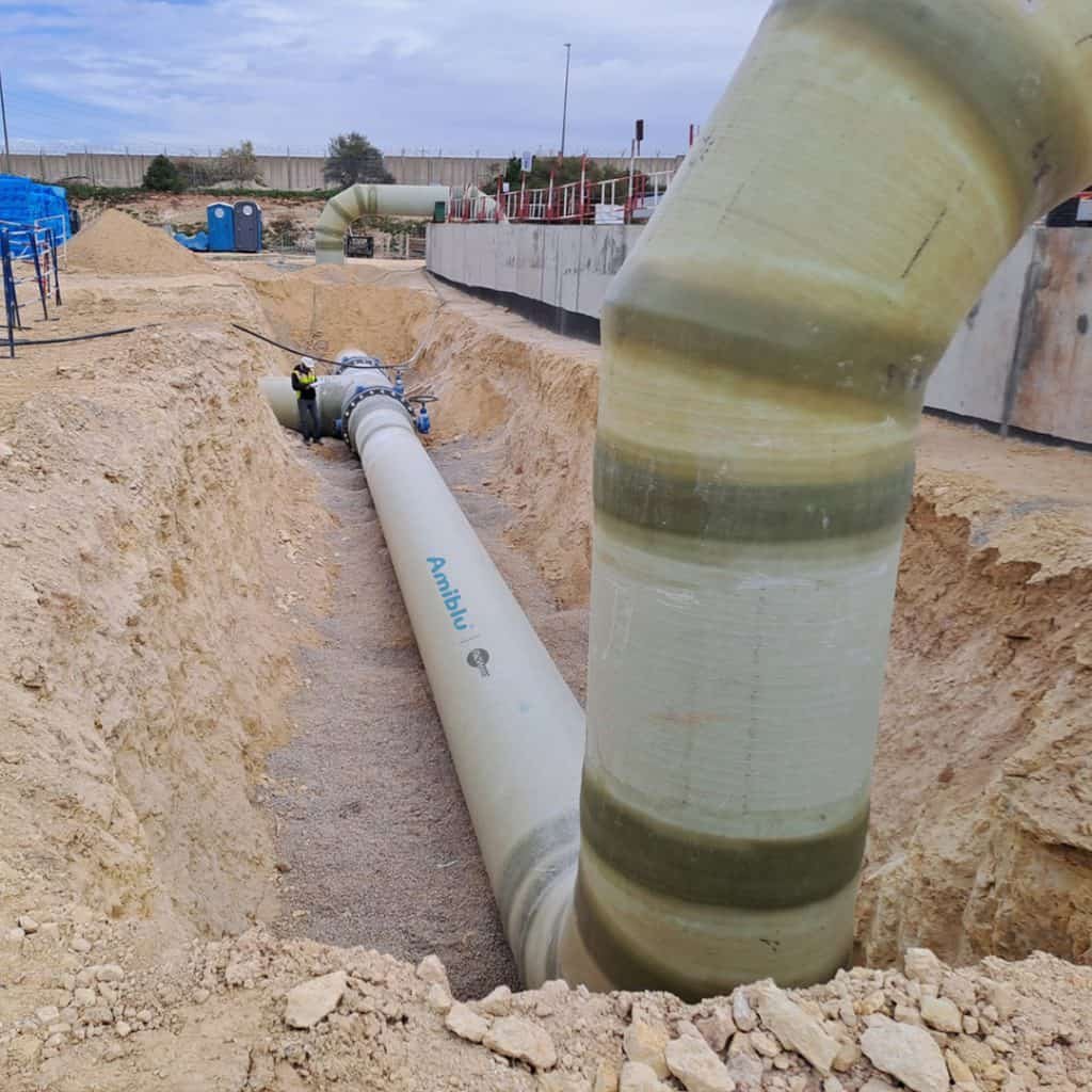 Large pipe under construction laid in a trench with equipment around; cloudy sky above.