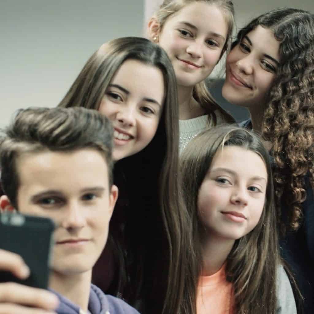 A group of five young people are harnessing technology as they gather to take a selfie, each beaming at the camera with smiles that reflect the joy of shared moments and digital connections.