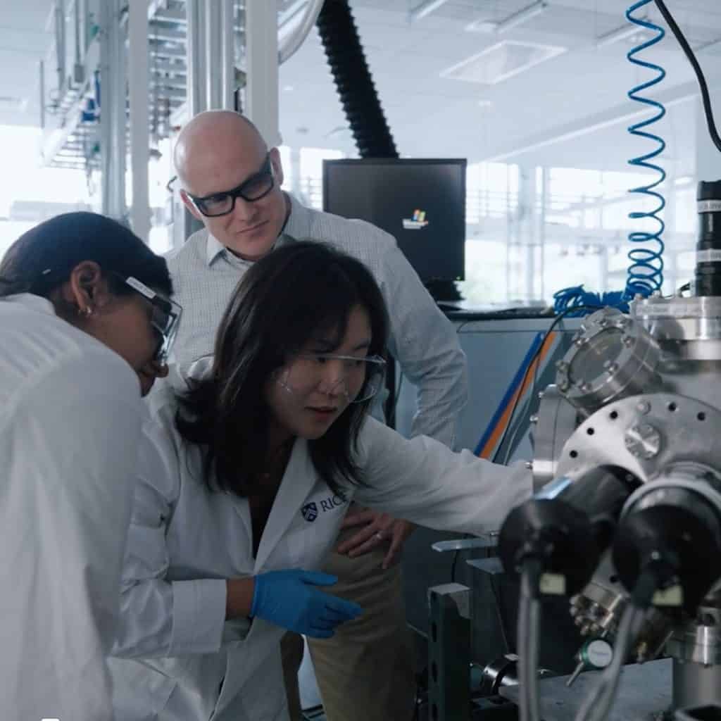 Three people wearing safety glasses work collaboratively with equipment in a Rice University laboratory setting.