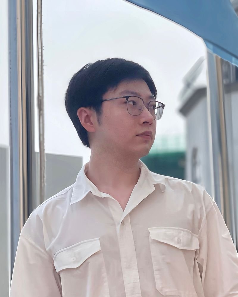 A person with glasses in a white shirt looks to the side, standing outdoors.