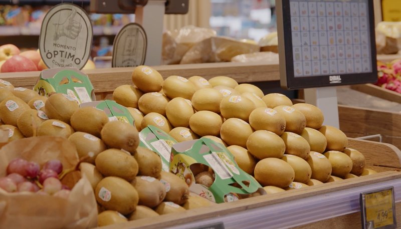 Display of kiwis and other fruits in a grocery store, with a digital scale in the background.