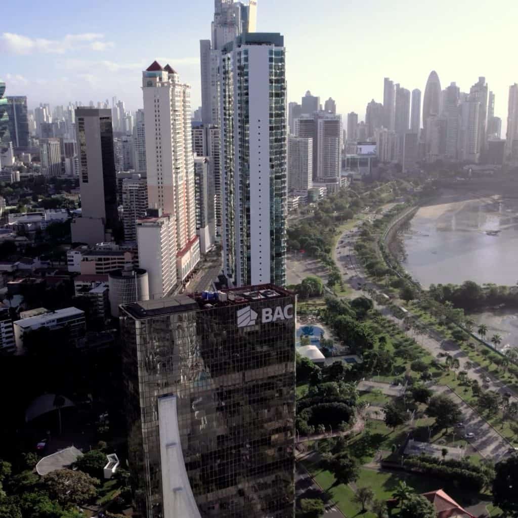 Aerial view of a cityscape with tall buildings and green spaces under a clear sky. The BAC building is prominent in the foreground.
