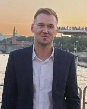 Dr. Zyrin, dressed in a sophisticated suit, stands by the river as the sunset sky paints a picturesque backdrop, accentuated by a majestic bridge.