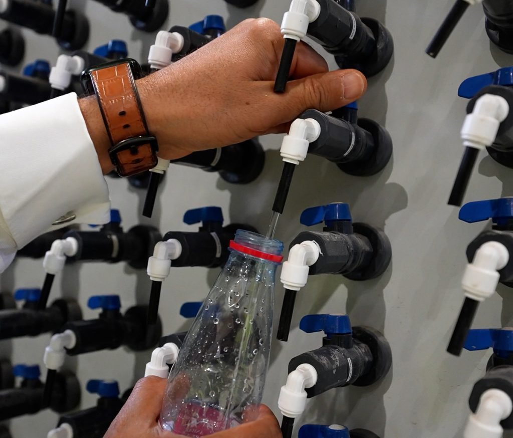 A person fills a plastic bottle with water from a set of pipes and valves, showcasing the efficient systems developed through the Saudi Water Partnership in Saudi Arabia.