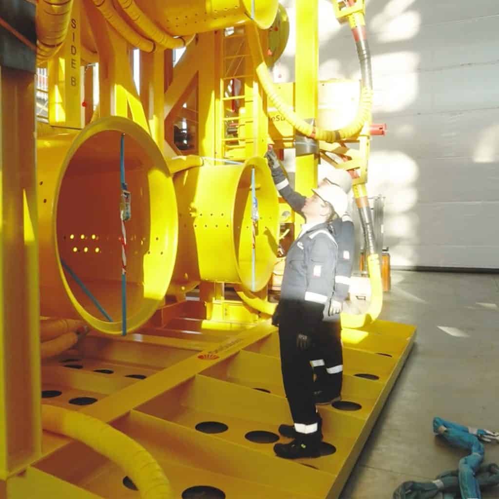 Two workers in safety gear examine large yellow industrial equipment inside a facility.